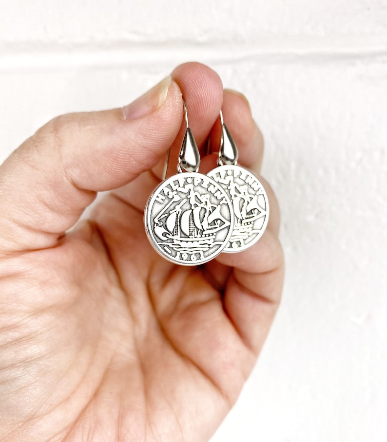 May include: Silver earrings shaped like a half penny coin with a ship design. The coin reads "HALF PENNY" and "1961".