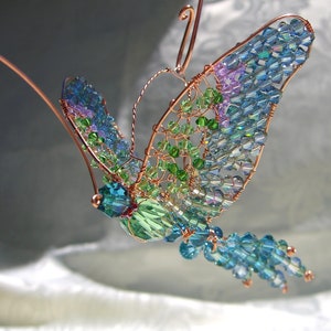 May include: A copper wire butterfly sculpture adorned with iridescent blue, green, and purple glass beads. The butterfly is suspended from a wire and features a delicate, intricate design.