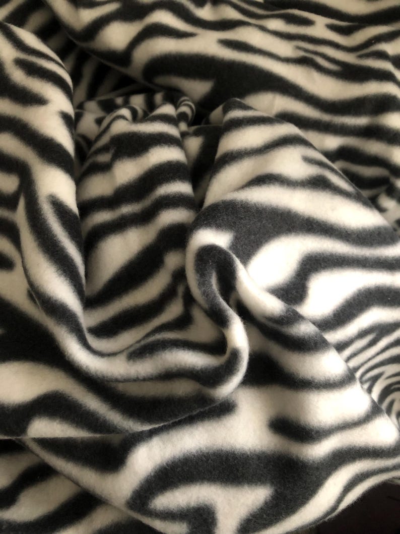 K&ouml;nnte beinhalten: Nahaufnahme eines gefalteten Stoffes mit Zebrastreifenmuster. Der Stoff hat abwechselnd schwarze und wei&szlig;e Streifen, die ein auff&auml;lliges Design ergeben. Das Material scheint weich und bequem zu sein, ideal f&uuml;r Decken.
