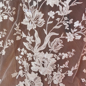 May include: White floral lace fabric with a delicate pattern of flowers and leaves. The lace is embellished with small sequins.
