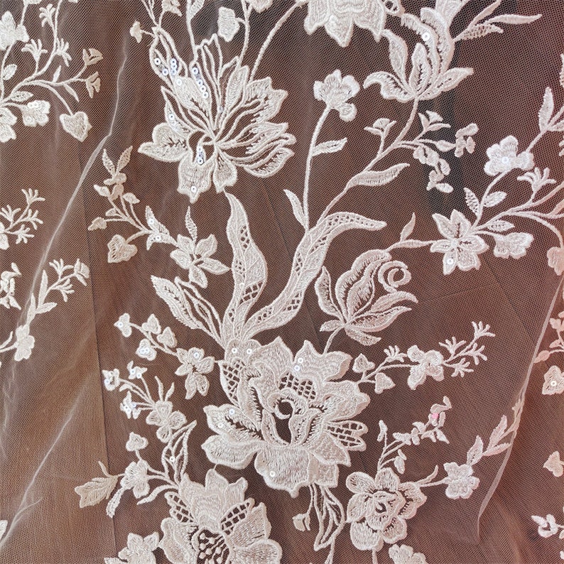 May include: White floral lace fabric with a delicate pattern of flowers and leaves. The lace is embellished with small sequins.