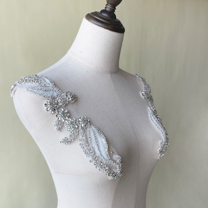 May include: A pair of white beaded embellishments with silver rhinestones, ideal for adding a touch of sparkle to a wedding dress or other formal attire.