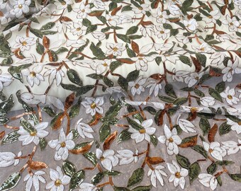Puede incluir: Tela marfil con estampado floral. Flores blancas con centros dorados y hojas verdes adornadas con lentejuelas. Los tallos y acentos marrones añaden contraste. Adecuado para prendas y proyectos decorativos.