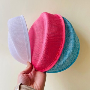 Op de afbeelding: Drie kleurrijke waszakken van mesh in wit, felroze en blauwgroen. De zakken worden bij elkaar gehouden en tonen hun afgeronde vorm en mesh-textuur. De blauwgroene tas heeft een blauwe rand.