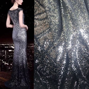 Peut inclure: Une robe longue sans manches avec un motif de paillettes argentées et noires. La robe a une silhouette ajustée qui s'évase légèrement vers le bas. Le tissu est drapé, mettant en valeur les paillettes scintillantes. En arrière-plan, un paysage urbain nocturne.