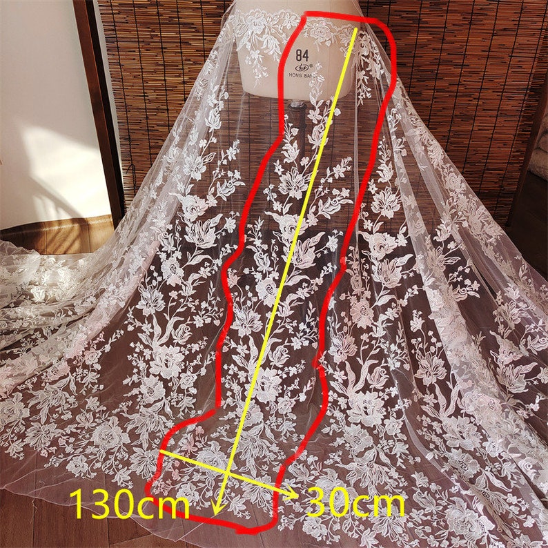 May include: White lace fabric with a floral pattern. The fabric is 130 cm wide and 30 cm long.