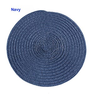 May include: A navy blue, round placemat with a woven texture. The placemat is made of a natural material and has a spiral design. The word "Navy" is printed in the upper left corner. This placemat is suitable for dining and home decor.