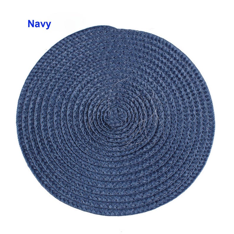 May include: A navy blue, round placemat with a woven texture. The placemat is made of a natural material and has a spiral design. The word "Navy" is printed in the upper left corner. This placemat is suitable for dining and home decor.
