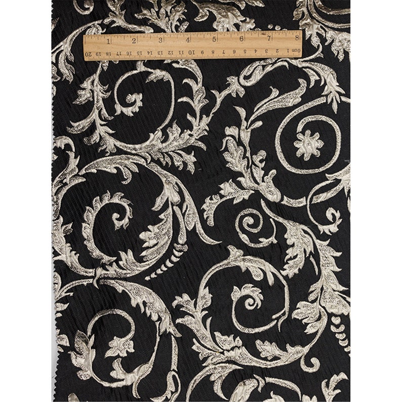 May include: Black fabric with a silver metallic floral pattern. The fabric has a textured, woven look.