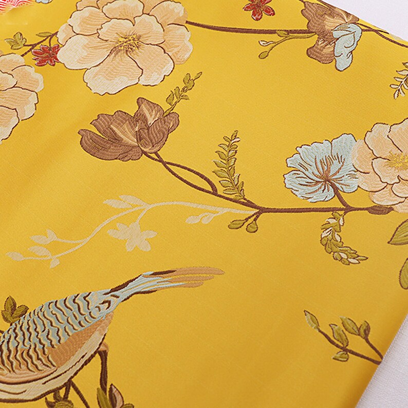 May include: Yellow fabric with a floral and bird design. The fabric features a light blue bird with brown and blue markings, and a floral pattern with light blue, brown, and white flowers.