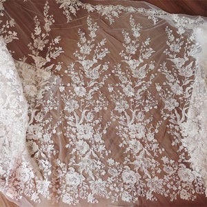 May include: White floral lace fabric with a delicate pattern. The lace is sheer and has a soft, flowing texture.