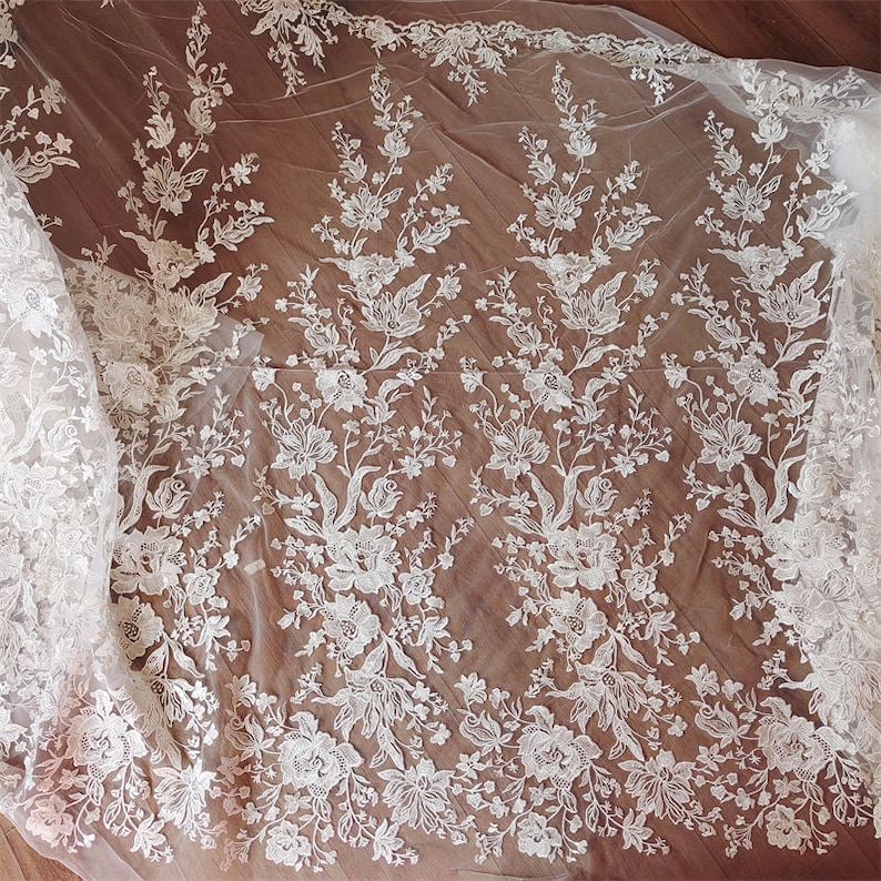 May include: White floral lace fabric with a delicate pattern. The lace is sheer and has a soft, flowing texture.