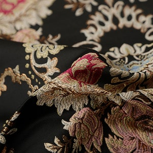 May include: Close-up of a black fabric with a gold, pink, and white floral pattern. The fabric has a textured, woven look.