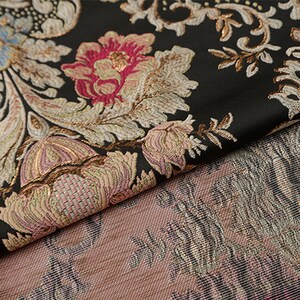 May include: Black fabric with a floral pattern in shades of pink, gold, and white. The fabric has a textured, woven look.