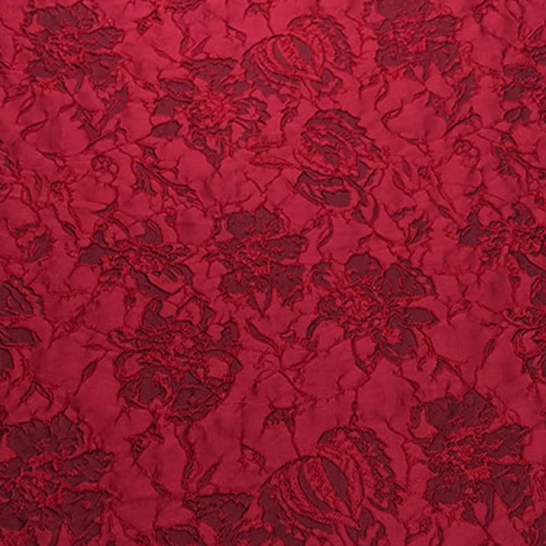 May include: Red fabric with a raised floral pattern. The fabric has a textured, embossed look.
