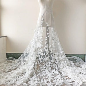 May include: White floral lace fabric with 3D flowers. The lace is delicate and intricate, with a soft, flowing texture. The flowers are white and have a realistic appearance.