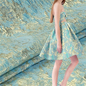 May include: A strapless dress and matching top in a textured fabric with a blue and gold pattern. The dress has a flared skirt and the top has a small bow detail. The fabric is draped in the background.