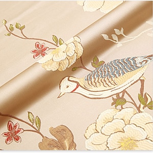 May include: Beige fabric with a floral and bird pattern. The fabric features white flowers, green leaves, and a brown and blue bird.