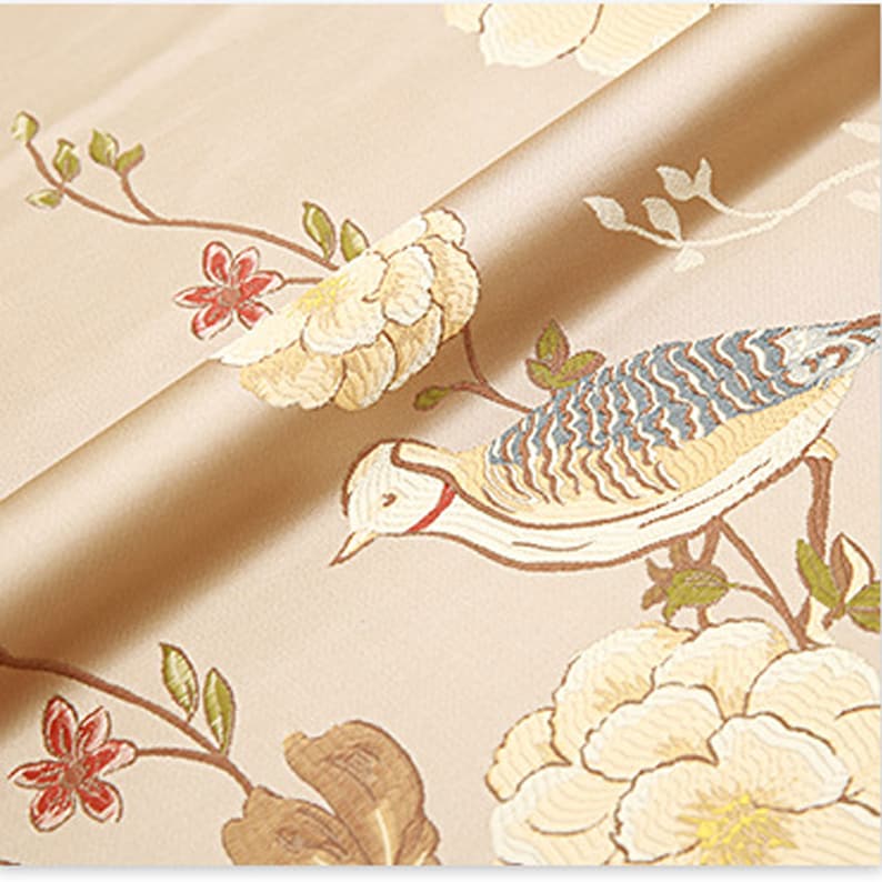 May include: Beige fabric with a floral and bird pattern. The fabric features white flowers, green leaves, and a brown and blue bird.