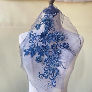 May include: A blue floral applique with pearl and rhinestone embellishments on a sheer mesh fabric. The applique is perfect for adding a touch of elegance to clothing, accessories, or home decor.