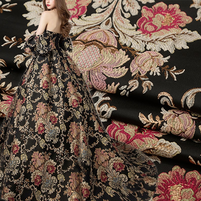 May include: Black fabric with a gold and pink floral brocade pattern. The fabric is draped over a dress with a similar pattern.