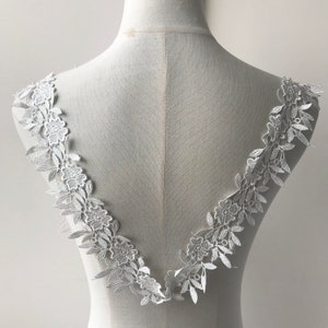 May include: White lace trim with a floral design. The trim is shown on a dress form and is perfect for adding a touch of elegance to any garment.