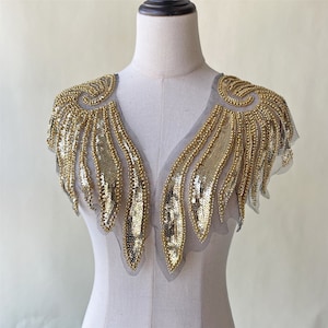 May include: Gold sequined and beaded embellishment for clothing. The embellishment is shaped like a V-neck and has a fringe design.