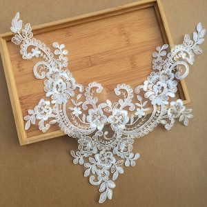 Pode incluir: Aplique de renda branca com um design floral. A renda é delicada e intrincada, com pequenas flores e folhas. O aplique é perfeito para adicionar um toque de elegância a qualquer peça de roupa.