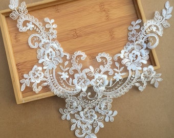 Può includere: Applique in pizzo bianco con un motivo floreale. Il pizzo è delicato e intricato, con piccoli fiori e foglie. L'applique è perfetta per aggiungere un tocco di eleganza a qualsiasi capo.