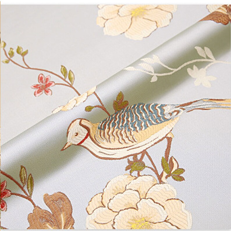 May include: A light blue fabric with a white and brown floral pattern and a bird with blue and brown feathers. The fabric has a subtle sheen and a soft texture.