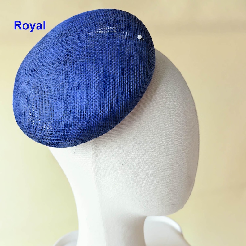 May include: A royal blue, oval-shaped hat with a textured weave. The hat is adorned with a small, white pearl and the word "Royal" is printed in blue. This headwear is likely suitable for special occasions.
