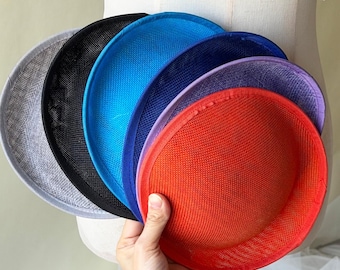 Könnte beinhalten: Eine Sammlung farbenfroher, runder Hutbasen in verschiedenen Farbtönen, darunter Grau, Schwarz, Blau, Lila und Rot. Die Hutbasen bestehen aus einem gewebten Material und werden auf einer Schaufensterpuppe präsentiert.