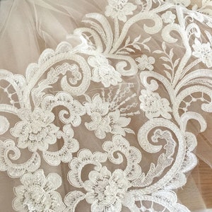 May include: White lace fabric with a floral design. The lace is delicate and intricate, with small flowers and leaves.