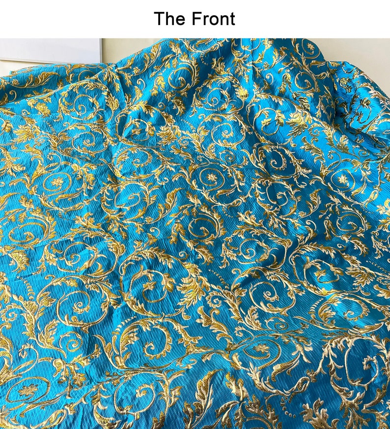 May include: A close-up of a blue fabric with a gold floral pattern. The fabric has a textured, woven look.