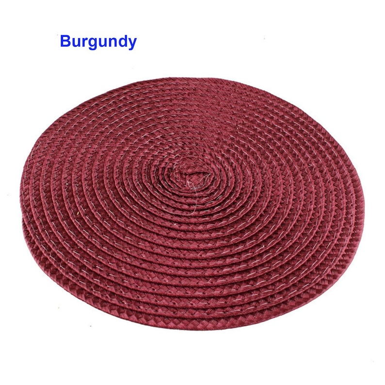 May include: A round burgundy placemat with a woven texture. The placemat is circular, with a spiral design radiating from the center. The word "Burgundy" is printed in blue in the upper left corner.