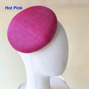 May include: A hot pink, oval-shaped hat with a textured surface. The hat is displayed on a white mannequin head. The text "Hot Pink" is visible in the upper left corner. This hat is suitable for special occasions.