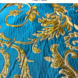 May include: Close-up of a teal fabric with a gold embroidered floral pattern. The fabric has a textured, woven look.