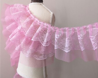 May include: Pink lace trim with a ruffled design. The trim is made of delicate lace and tulle, and it has a soft, feminine look.
