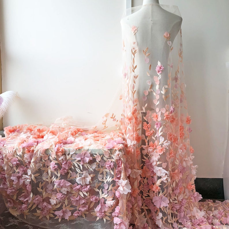 May include: Pink and peach floral lace fabric with 3D flowers. The fabric is sheer and delicate, with a soft, romantic feel.