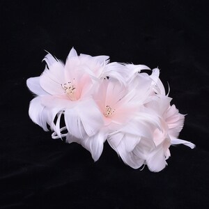 May include: A delicate white feather flower with pink accents. The flower is made of soft feathers and has a delicate, feminine look.