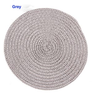May include: A round, grey woven placemat. The placemat is made of a braided material and has a spiral design. The word "Grey" is in the upper left corner.