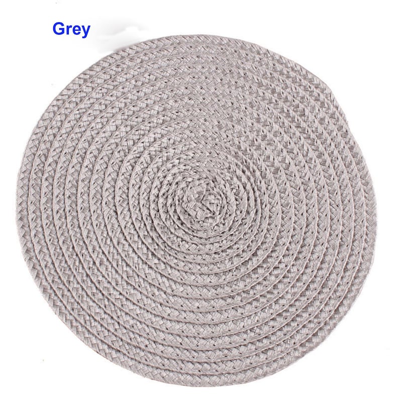 May include: A round, grey woven placemat. The placemat is made of a braided material and has a spiral design. The word "Grey" is in the upper left corner.