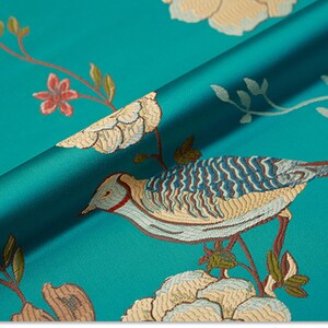 May include: Teal fabric with an embroidered design of birds, flowers, and leaves. The fabric has a satin-like sheen.