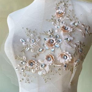 Può includere: Un'applicazione floreale delicata con fiori beige e strass scintillanti. L'applicazione è perfetta per aggiungere un tocco di eleganza a vestiti, accessori o arredamento per la casa.
