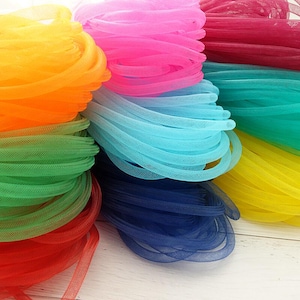 Könnte beinhalten: Eine Sammlung von aufgerollten, hohlen, röhrenförmigen Netzbändern in einer Vielzahl lebendiger Farben wie Orange, Pink, Magenta, Türkis, Hellblau, Grün, Gelb, Rot und Dunkelblau mit einer feinen, halbtransparenten, gewebten Textur.