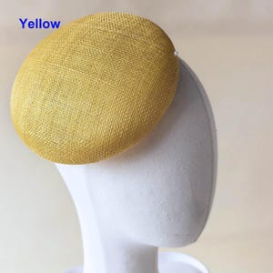May include: A yellow, oval-shaped hat with a textured surface. The word "Yellow" is printed in blue in the upper left corner. The hat is displayed on a white mannequin head.