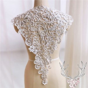 May include: White lace collar featuring a delicate floral design. The collar is crafted from a sheer fabric with a scalloped edge. It's ideal for adding a touch of elegance to any outfit.