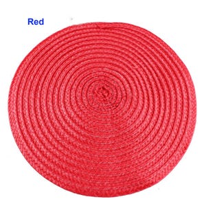 May include: A round, red placemat with a woven design. The placemat is circular and made of a tightly woven material. The word "Red" is in the upper left corner. This placemat is suitable for dining and kitchen decor.