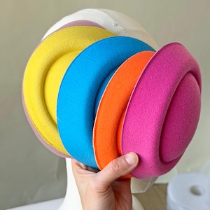 Puede incluir: Un sombrero multicolor con un diseño redondeado. El sombrero presenta bandas de color amarillo, azul, naranja y rosa, sobre una base blanca. El diseño muestra una disposición lúdica de colores y texturas, adecuado como accesorio de moda.