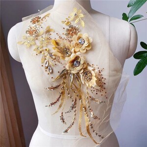 May include: Gold floral applique with sequins and rhinestones. The applique is on a sheer fabric background.